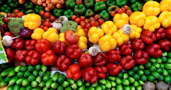 A stand with vegetables such as yellow pepper, beetroot, tomatoes, cucumber, pumpkin, carrots, radish, beetroot, garlic.